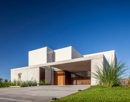 Fachada moderna de hormigón blanco y gris con vegetación alta — proyecto CASA J2M, por GMARQ, en Belén de Escobar