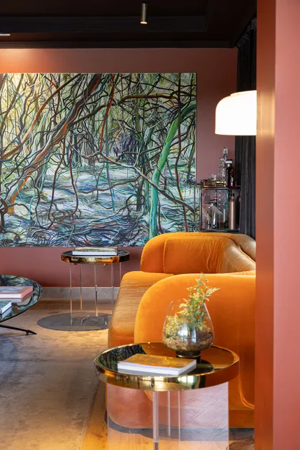 Sala de estar moderna con sofá naranja, pintura de bosque y mesas acrílicas — proyecto C'est Moi , por Gaby Alfonso, en B1648 Tigre