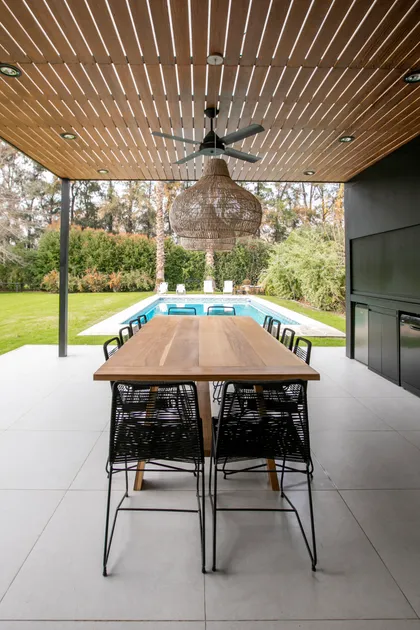 comedor exterior moderno con mesa de madera y sillas de mimbre junto a piscina — proyecto Obra Newman J, por Arq. Lourdes Yarade Saravia, en Benavidez