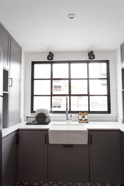 Cocina moderna con mesada blanca, muebles negros y gran ventanal industrial — proyecto Obra Olazábal II, por SYA Arquitectas, en Belgrano