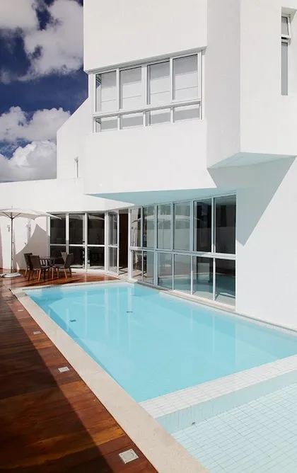 Casa moderna con pileta frente a fachada blanca y deck de madera — proyecto Casa em Garanhuns Pernambuco, por André Caricio