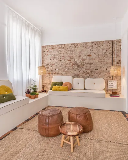 Dormitorio minimalista con pared de ladrillo, cama blanca y puffs de cuero — proyecto Roomie Coliving, por Camila Cavalheiro Arquiteta