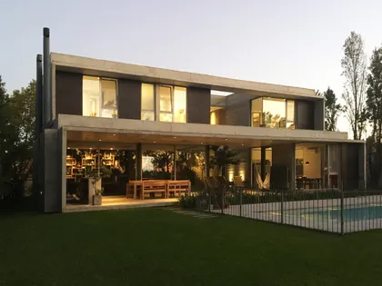Casa contemporánea de dos plantas con fachada gris y vidrio, atardecer — proyecto Casa en Santa Barbara, por Crea Constructora, en Benavidez