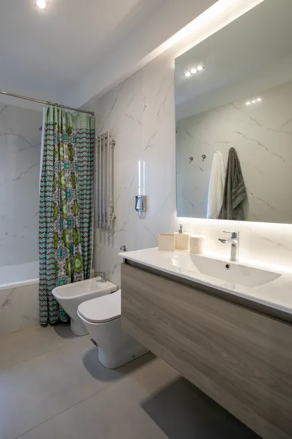 Baño moderno con paredes de mármol, luz indirecta y vanitory de madera — proyecto Obra Araoz A, por Arq. Lourdes Yarade Saravia, en Buenos Aires