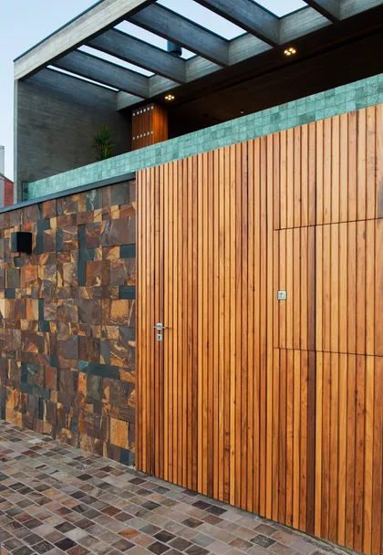 Fachada moderna con portón de madera y muro de piedra — proyecto CASA OCEANO, por Mayresse Arquitetura