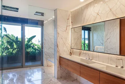 Baño moderno con vista a vegetación, paredes de mármol y vanitory de madera — proyecto Water House, por Remy Arquitectos, en Rincón de Milberg