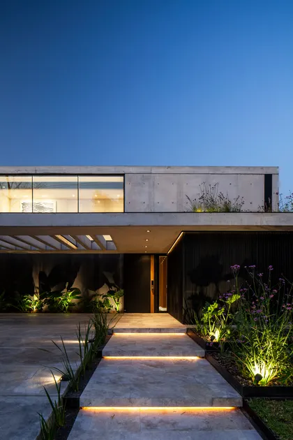 Fachada moderna de hormigón con luces integradas y vegetación exuberante — proyecto CASA AH, por GMARQ, en Garin