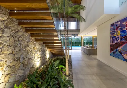 Pasillo moderno con escalera de madera, muros de piedra y plantas colgantes — proyecto Casa D.M.G., por Ruschel Arquitetura e Urbanism