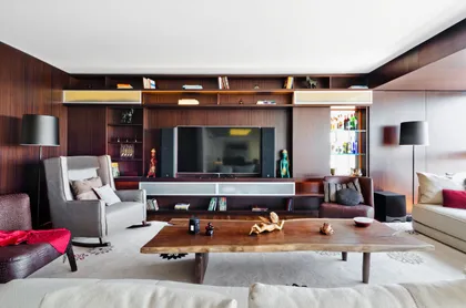 Living moderno con paneles de madera oscura y muebles grises — proyecto Departamento Nuñez, por Claudia Faena Studio, en Núñez