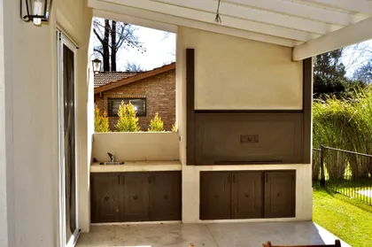 Quincho moderno con parrilla integrada y mesada de madera — proyecto Newman Benavidez, por Marconi Silva Arquitectos, en Benavidez