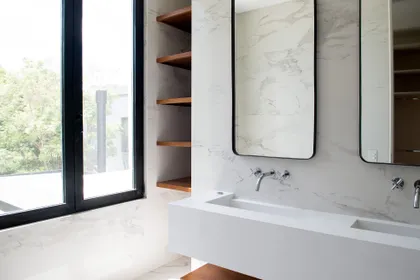 Baño moderno con mesada de mármol, vanitory doble y estantes de madera oscura — proyecto Bosque Chico, por Estudio Arq. María Sioli, en Garin