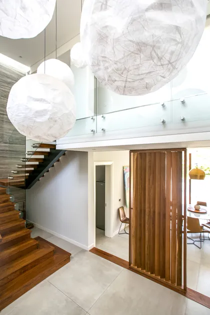 Escalera de madera y pasillo doble altura con lámparas colgantes blancas — proyecto PGC-01, por VGLA Arquitectos, en General Pacheco
