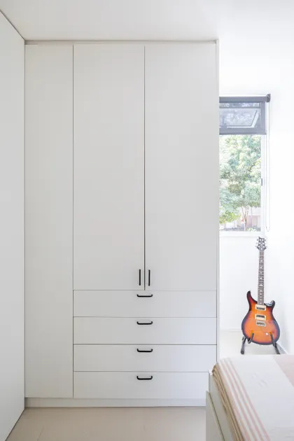 Dormitorio minimalista con placard blanco, guitarra eléctrica y ventana luminosa — proyecto Apartamento 407N, por Coda Arquitetos