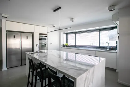 Cocina moderna con isla grande de mármol y ventanas hasta el techo — proyecto Obra Montevideo, por Arq. Lourdes Yarade Saravia, en Buenos Aires