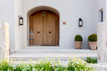 Fachada mediterránea con puerta de madera arqueada y topiarios — proyecto Casa MF, por Estudio Junor, en Belén de Escobar