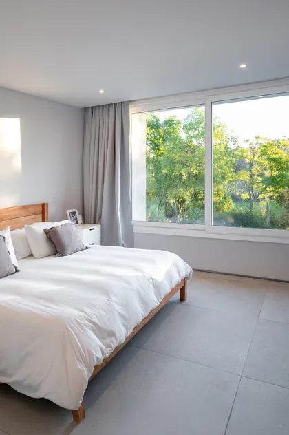 Dormitorio minimalista con grandes ventanales y vista al bosque — proyecto Campo grande I, por Juarez-Fevre Estudio de Arquitectura , en Pilar