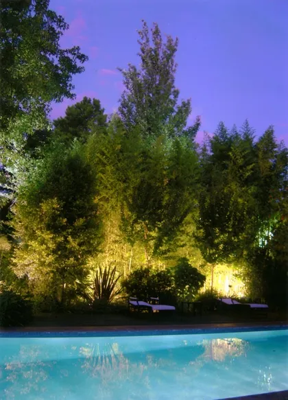Pileta iluminada en jardín con vegetación exuberante al anochecer — proyecto Iluminacion de fachadas, por Estudio Parisio & asoc., en Pilar