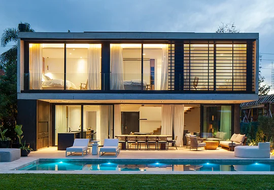 Fachada moderna iluminada con piscina y deck — proyecto Casa GMARQ, por Aluar División Elaborados