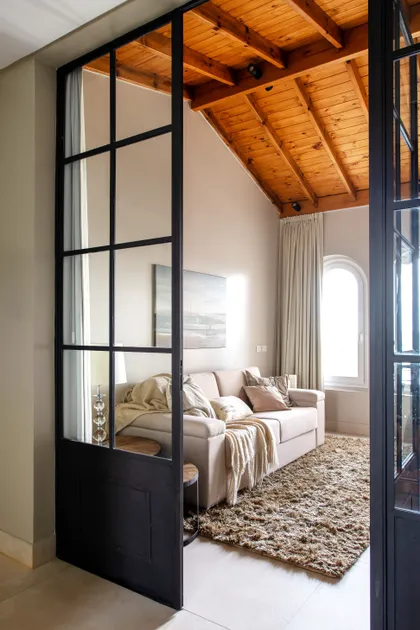 Living con techo de vigas de madera expuestas y puerta divisoría industrial — proyecto Casa MF, por Estudio Junor, en Belén de Escobar