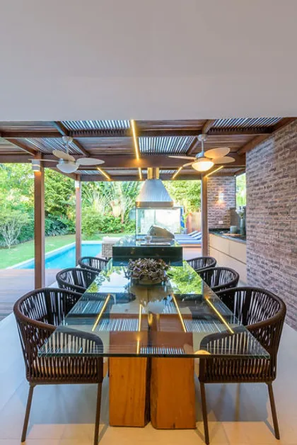 Galeria techada con comedor, sillas de ratan y pileta de fondo — proyecto Casa De Praia, por Bordin E Soares Interiores