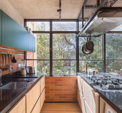 Cocina industrial con ventanal grande, ladrillo visto y muebles de madera — proyecto Apartamento SQN 410, por Coda Arquitetos