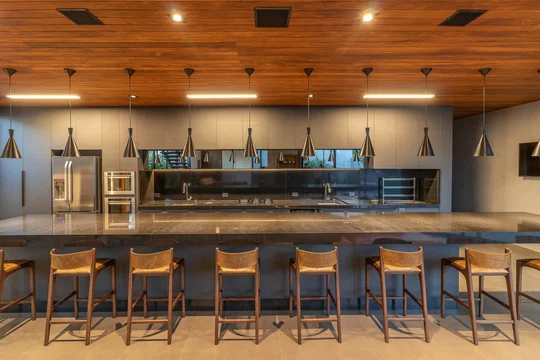 Comedor moderno con barra isla y luces colgantes sobre piso de madera — proyecto Casa CaCle, por Studio Jordano Valota