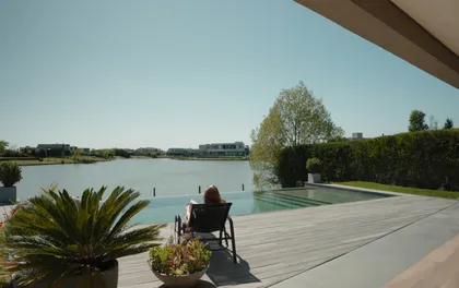 Piscina moderna con deck de madera junto a espejo de agua y vegetación — proyecto Panorama House, por Estudio UFV72, en Belén de Escobar