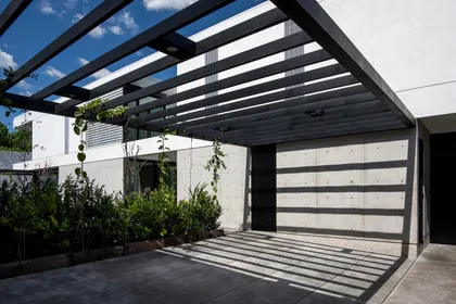 Fachada moderna con pérgola de metal negro y hormigón texturizado — proyecto CASA SD28, por GMARQ, en Buenos Aires