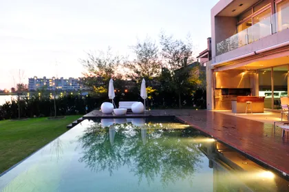 Piscina infinita moderna con mobili blancos al atardecer — proyecto Casa AB, por Santiago Cordeyro Arquitectos, en Nordelta