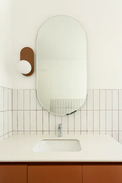 Baño moderno con espejo ovalado, lavabo blanco y mueble terracota — proyecto CASA CC, por Rastro Estudio, en San Isidro