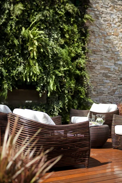 Living exterior moderno con pared verde, muebles de mimbre y deck de madera — proyecto Alto de Pinheiros I, por Deborah Roig