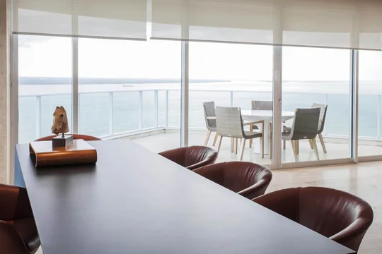 Oficina ejecutiva con vista panorámica al mar, mesa curva y sillas de cuero — proyecto Cobertura LS, por Patrícia Marinho Arquitetura 