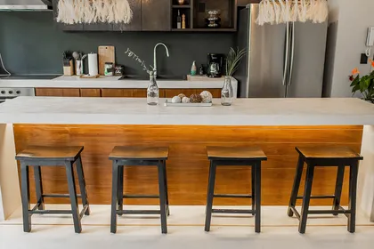Cocina moderna con isla de madera y taburetes negros — proyecto Tropical Moroccan Paradise, por Interiors Tulum