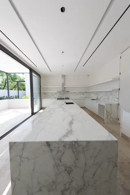 Cocina moderna con isla grande de mármol y ventanales amplios — proyecto Casa C, por Estudio Dado, en Belgrano