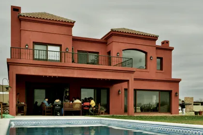 Casa moderna terracota con piscina y gente en galería — proyecto San Marcos 2, por Marconi Silva Arquitectos, en Benavidez