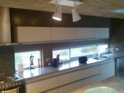 Cocina moderna minimalista con muebles blancos, hormigón y detalles metálicos — proyecto VILLA ESMERALDA, por GJF estudio, en Pinamar