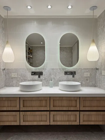 Baño moderno con doble bacha, espejos ovalados retroiluminados y muebles de madera — proyecto Lafinur, por MDBK Arquitectura, en Palermo