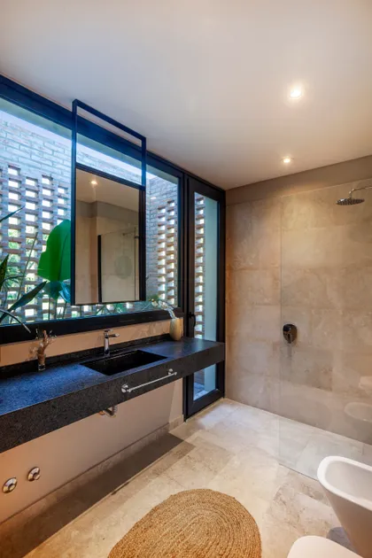 Baño moderno con mesada de piedra oscura, ventana y bañera exenta — proyecto Casa Brick, por LSA. , en Pilar