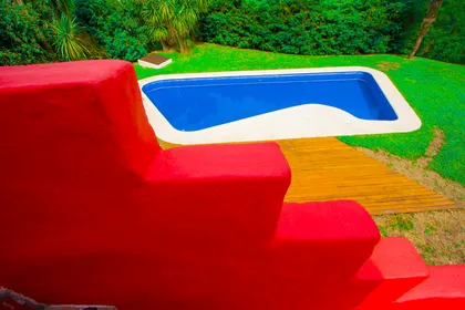 Escalera roja vibrante junto a piscina azul y jardín verde — proyecto Arquitectura, por Geo Estudio, en Buenos Aires