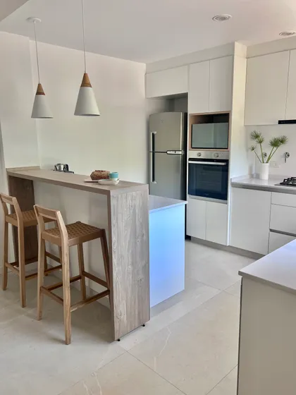 Cocina moderna con isla, taburetes de madera y luces colgantes — proyecto PH CASI, por Estudio Grupo 32, en San Isidro