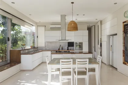 Cocina moderna con isla blanca, mesadas madera y grandes ventanales — proyecto Santa Barbara 121, por Build a Home Arquitectura, en B1648 Tigre
