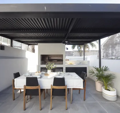 Comedor exterior moderno bajo pérgola negra con jardín y parrilla — proyecto PH Salguero, por Parq Estudio, en CABA