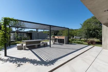Quincho moderno con pergola, parrilla integrada y deck de hormigon — proyecto Casa TT, por Grupo Studio, en Villa Allende