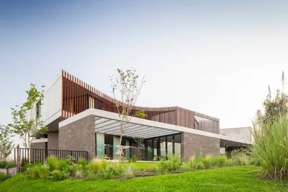 Fachada moderna de casa con madera, piedra y grandes ventanales — proyecto Casa Órbita, por Estudio PK, en Nordelta