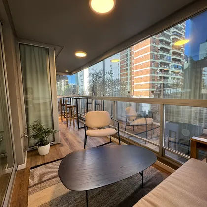 Balcón moderno con sillón beige, mesa negra y vista urbana — proyecto Salguero I, por MDBK Arquitectura, en Palermo