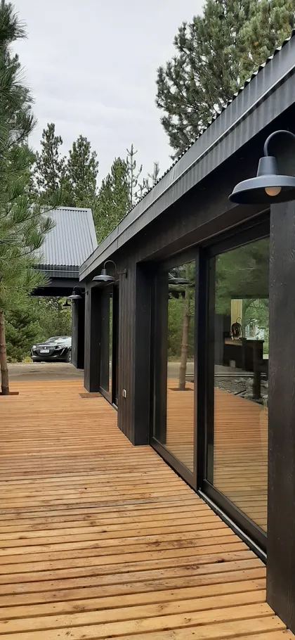 Fachada moderna de madera oscura con deck de madera y bosque — proyecto Casa LA MOROCHA, por Showhouse Bariloche, en San Carlos de Bariloche
