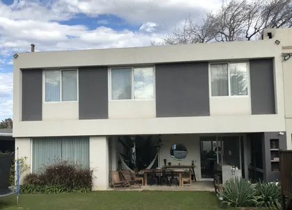 Fachada moderna con grandes ventanales y patio con muebles de rattan — proyecto LA HORQUETA, por Fb Arqs, en San Isidro
