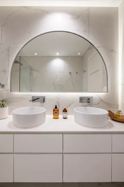 baño moderno con doble lavabo y espejo arqueado — proyecto AS, por Estudio Basa, en Buenos Aires