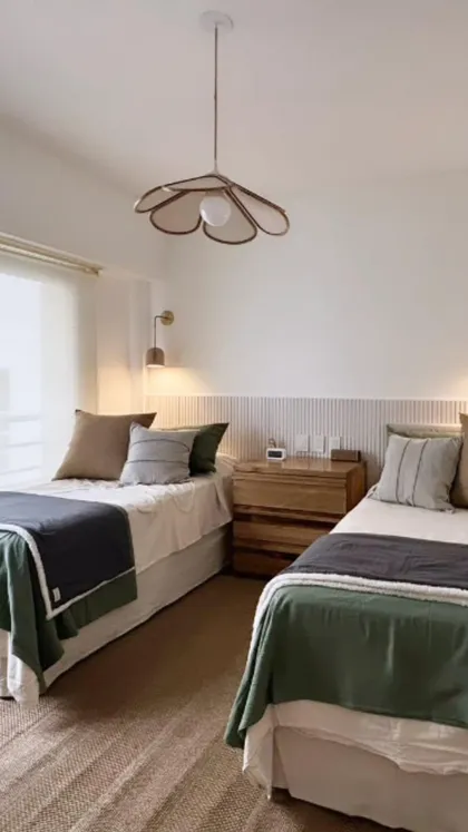 Dormitorio moderno con dos camas, lámpara floral y detalles en madera — proyecto Uruguay, por Claraboia , en Recoleta