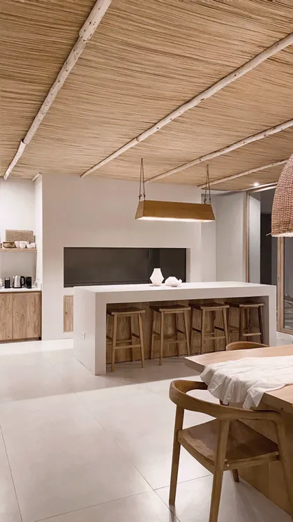 Cocina abierta estilo mediterráneo-boho con isla blanca y techo de caña — proyecto El Refugio, por Grupo Pauta Arquitectura, en Pinamar
